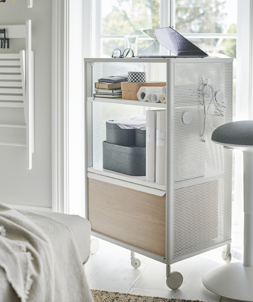 Използвай системата за съхранение на колелца IKEA BEKANT като мобилно бюро за домашния офис. Бяла мебел за съхранение на колелца с лаптоп върху нея, до прозорец.