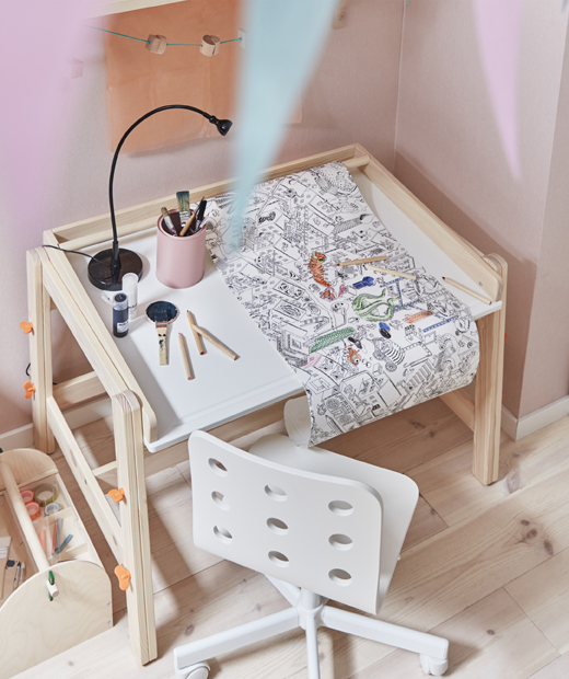Ролката с хартия за оцветяване IKEA LUSTIGT и детското бюро с променлива височина FLISAT, направени да растат с детето ви. Ролка с хартия за оцветяване върху детско бюро с бял стол до розова стена.