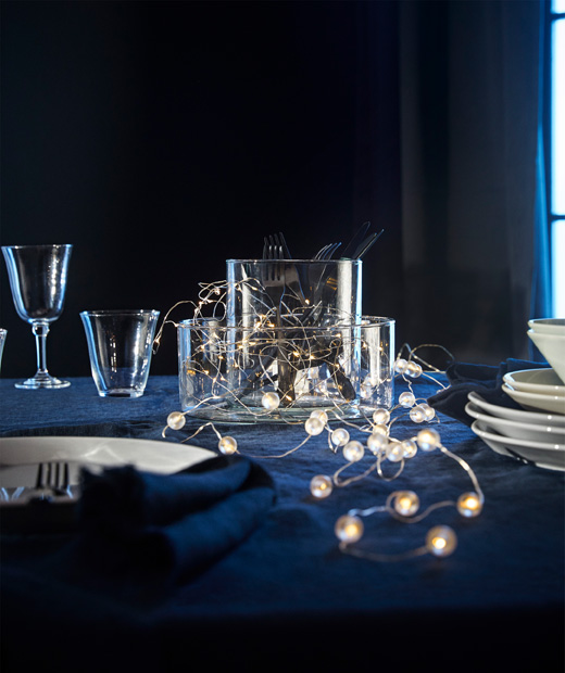 Гирлянд от LED крушки SNÖYRA върху маса с чаши, чинии и купи.